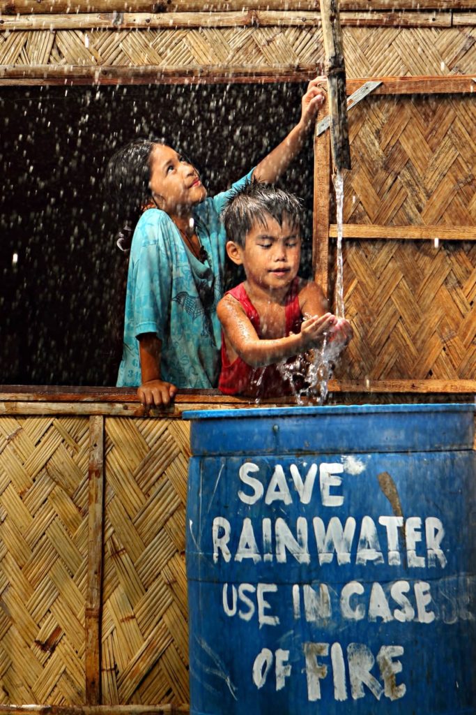 Children collecting rainwater from a large storage container used for fire prevention