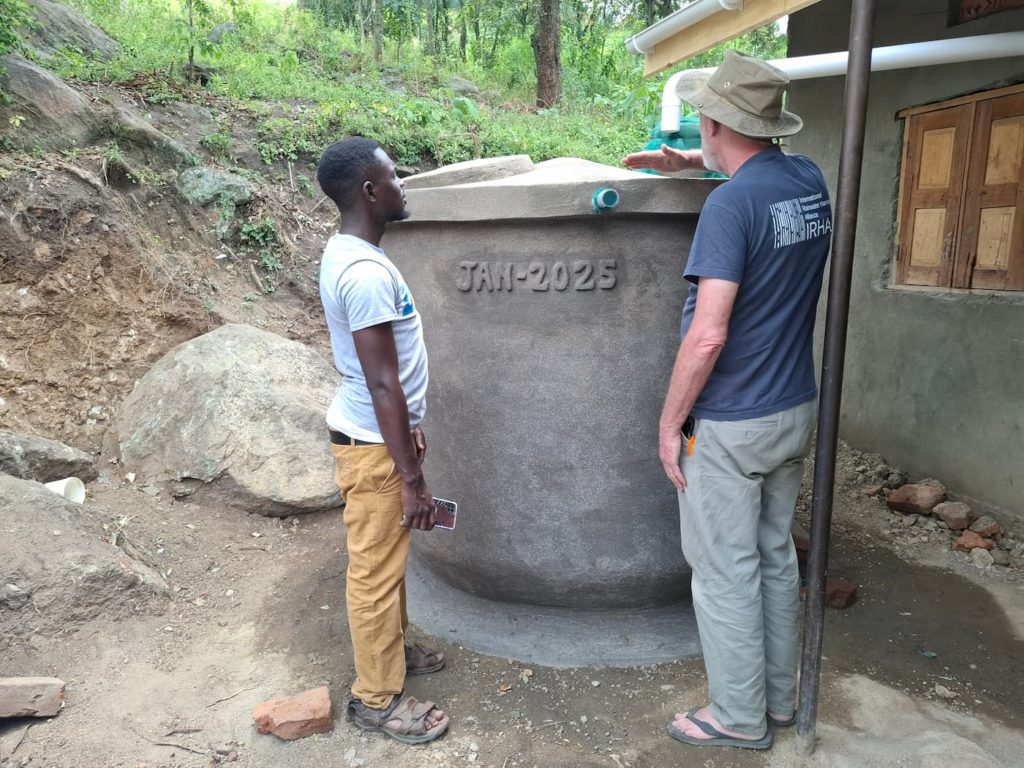 IRHA president sharing rainwater tank knowledge with a senior mason in Uganda