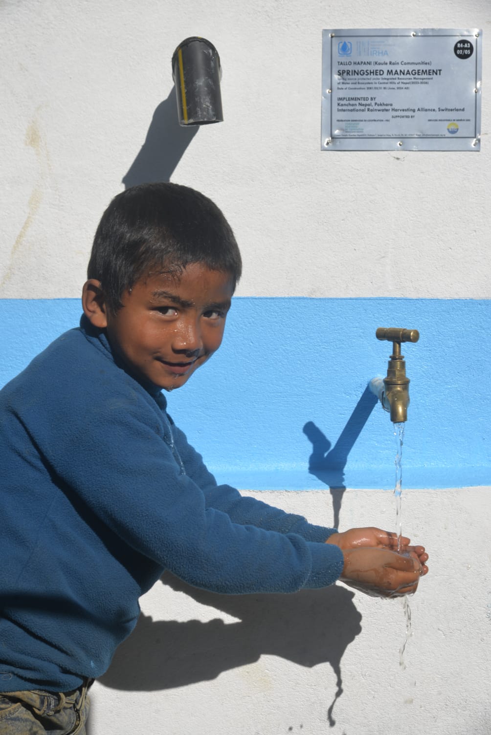 Boy collecting water with his hands from a rainwater tank through water improved access in Nepal