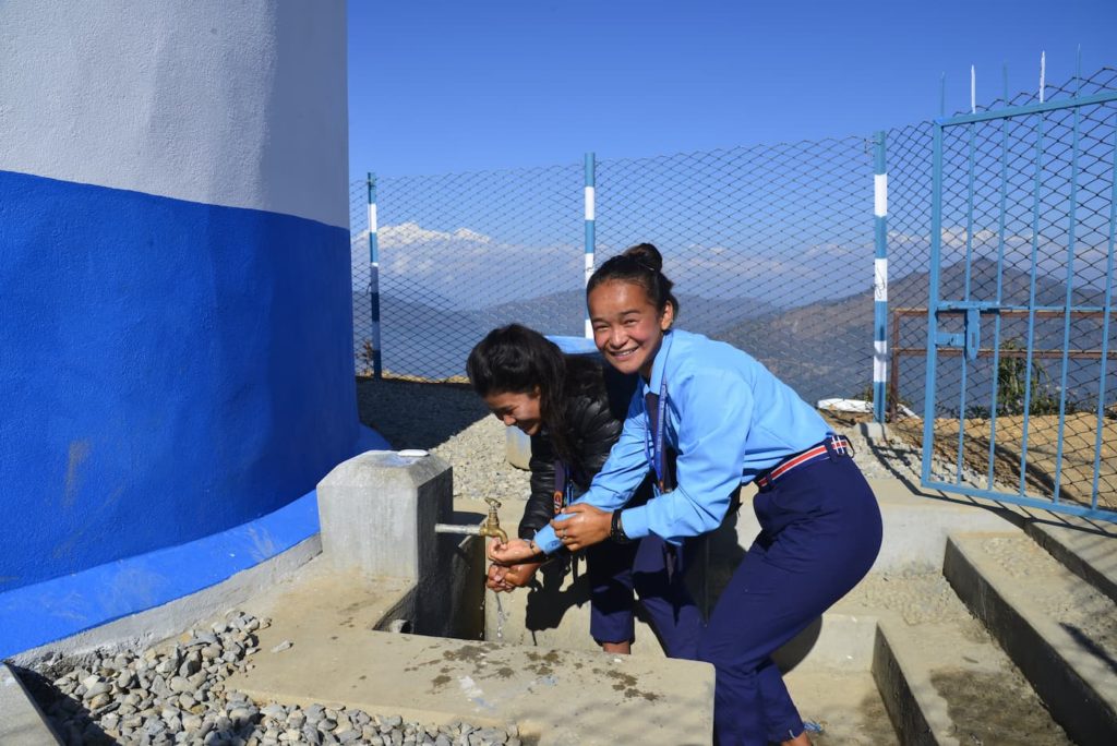 Schoolgirls drinking water from a rainwater harvesting tank at a school in Nepal