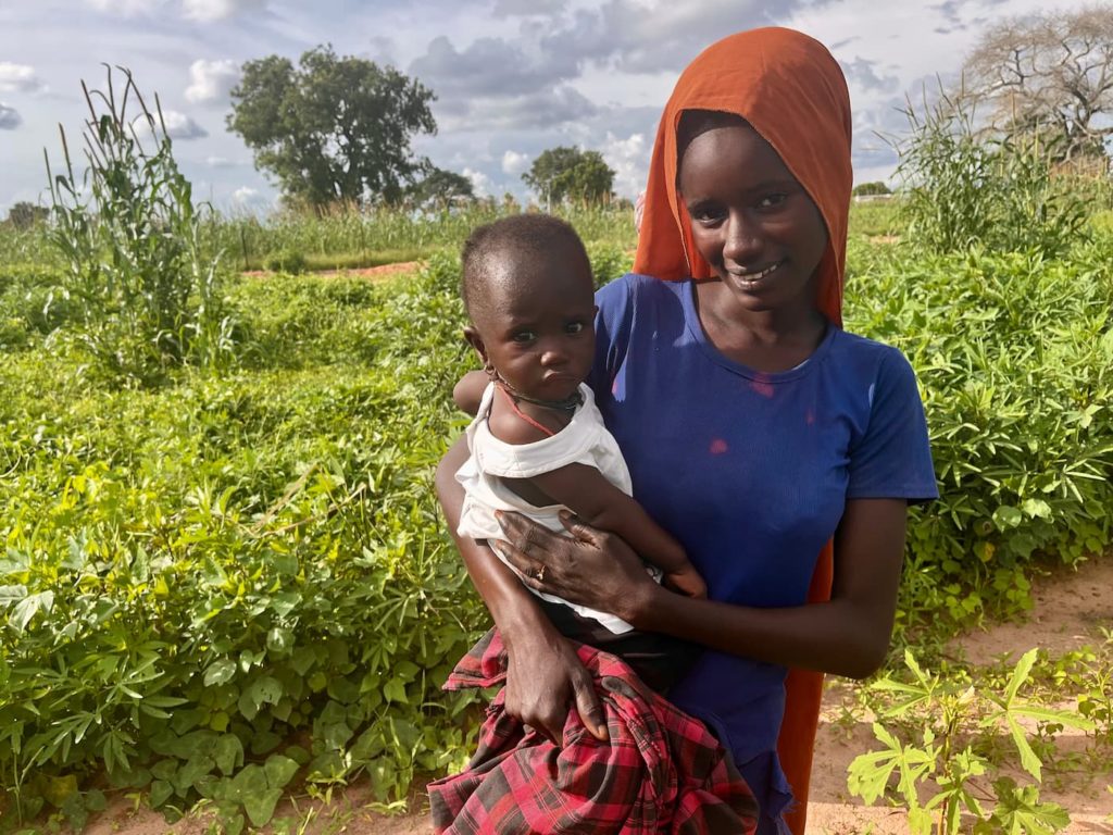 Woman farmer in Senegal holding her young child and smiling in her field