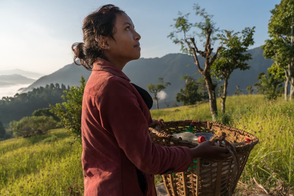 Sushmita carrying a water basket while looking up at the sky during her journey in Nepal